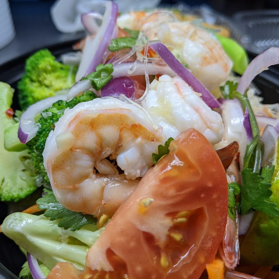 Close-up of a vibrant Thai salad with shrimp, broccoli, red onion, and tomato slices.